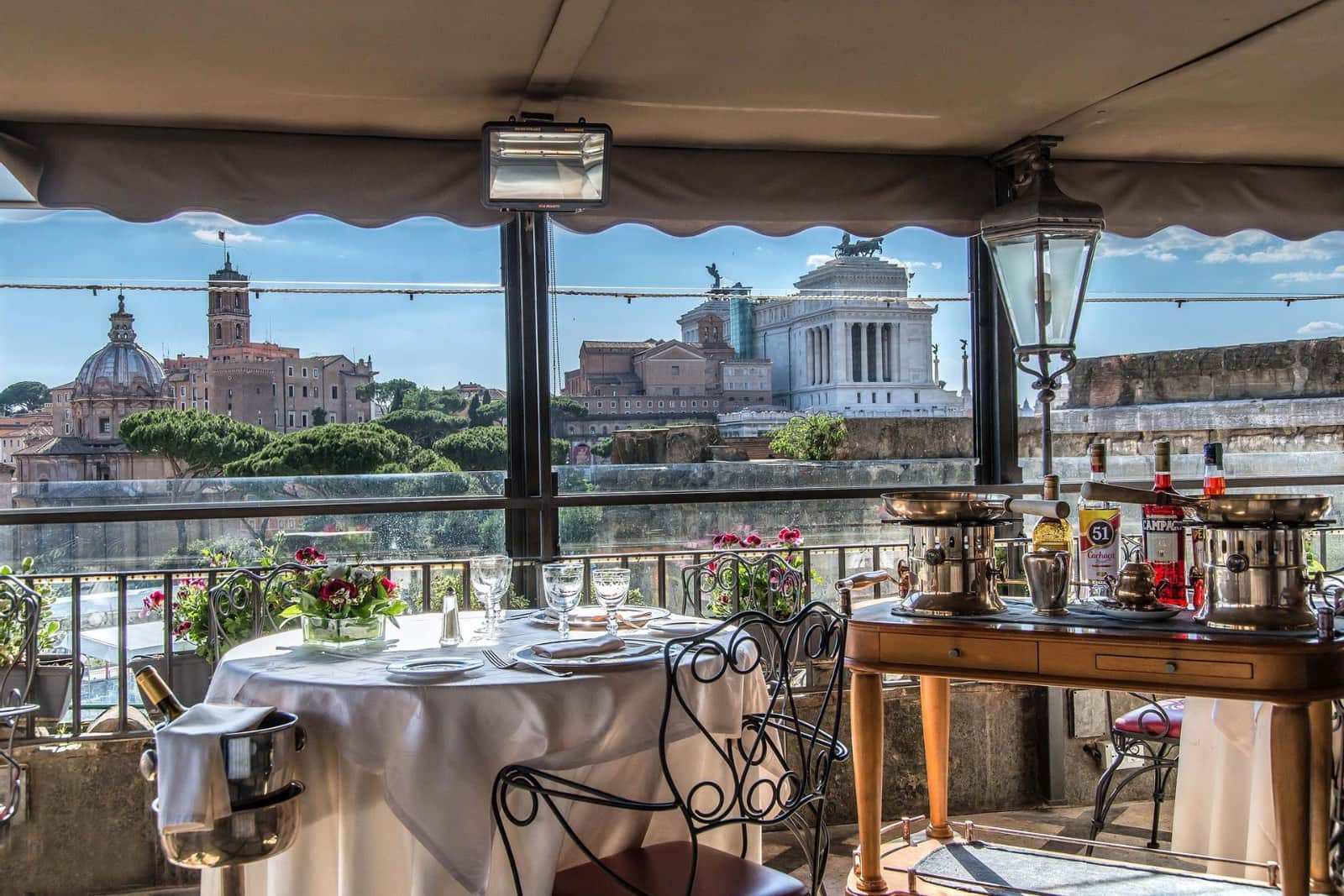 Terrazza coperta con tavolo apparecchiato e vista sui tetti di Roma e sull'Altare della Patria.